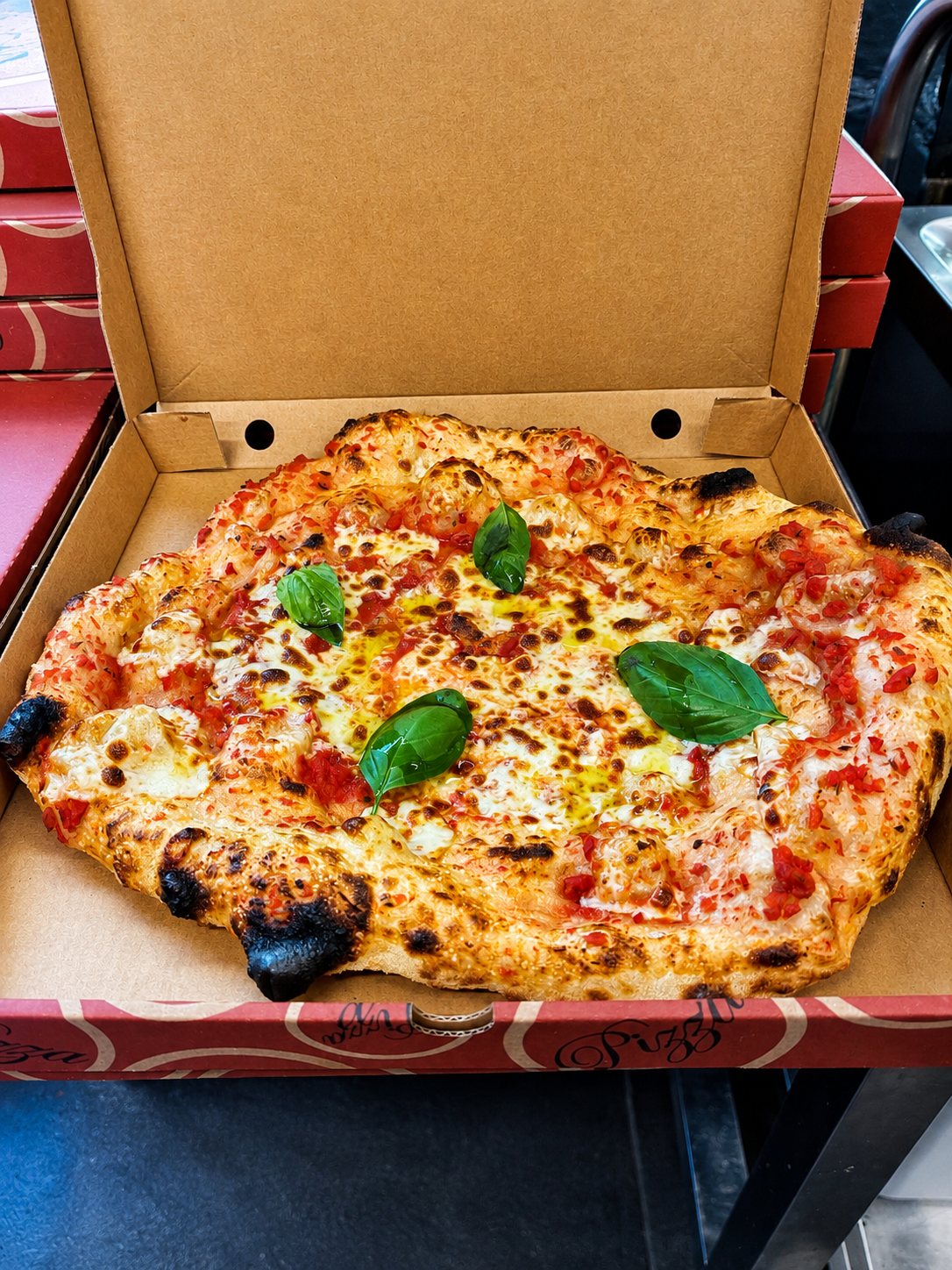 Pizza margherita au basilic frais dans sa boîte, bord gonflé et alvéolé