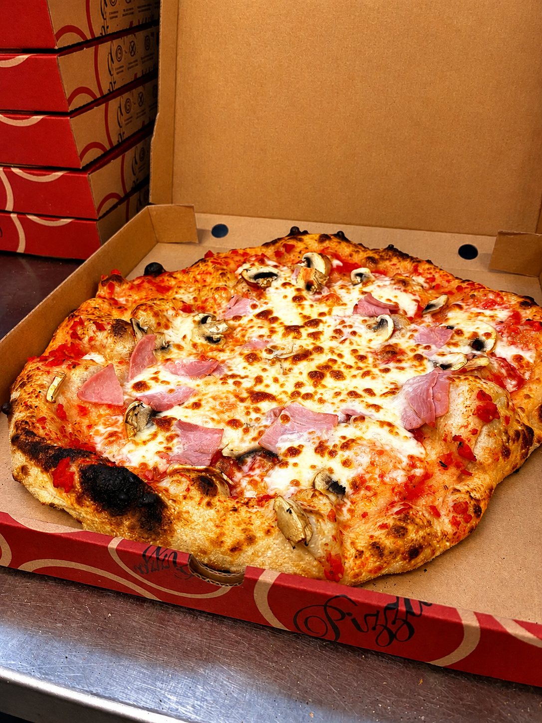 Pizza reine dans sa boîte : jambon, champignons, bord alvéolé